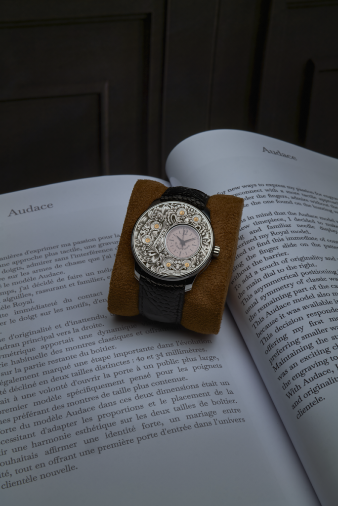 Gros plan sur une montre-bracelet de luxe RBaptiste. Le cadran est une œuvre d'art complexe, symétriquement gravée à la main au burin avec des motifs ornementaux et des accents dorés. Boîtier en acier poli et bracelet noir texturé. Sur un fond d'écrin flou.
