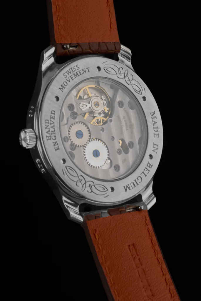 Vue de dos d'une montre de luxe RBaptiste avec fond transparent dévoilant le mouvement mécanique. Le pourtour du boîtier présente les gravures "Made in Belgium", "Hand Engraved" et des motifs floraux réalisés à la main par l'horloger créateur.