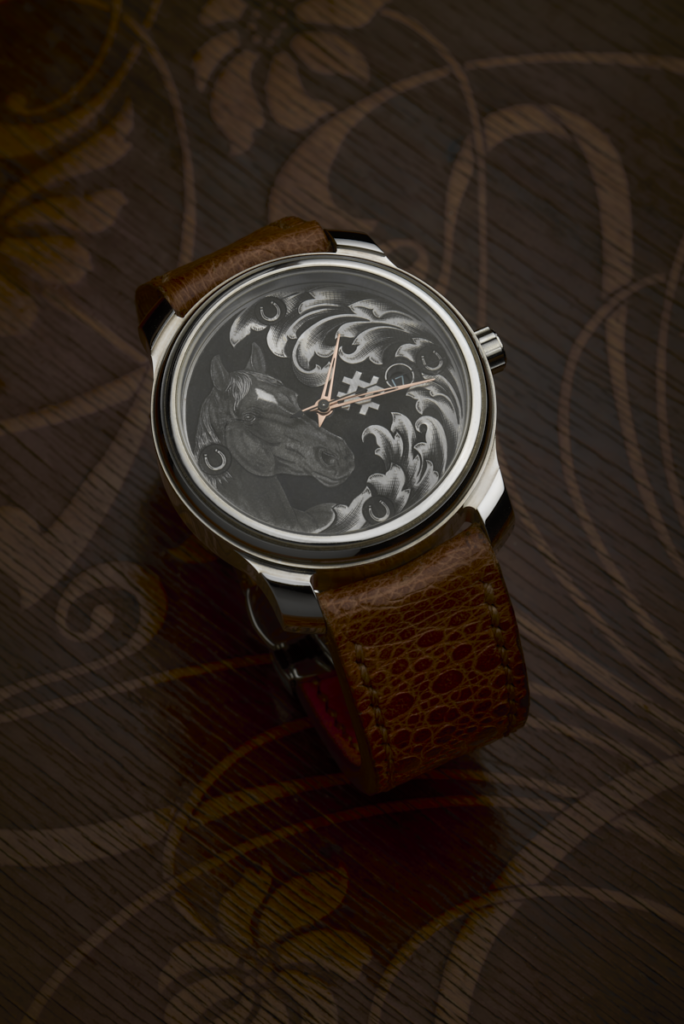 Montre RBaptiste par Roland Baptiste, horloger créateur. Cadran sombre orné d'une minutieuse gravure asymétrique réalisée à la main au burin, aiguilles dorées et bracelet en cuir brun texturé.